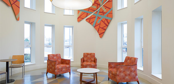 A common area in the building with orange arm chairs, a coffee table and art on the walls.